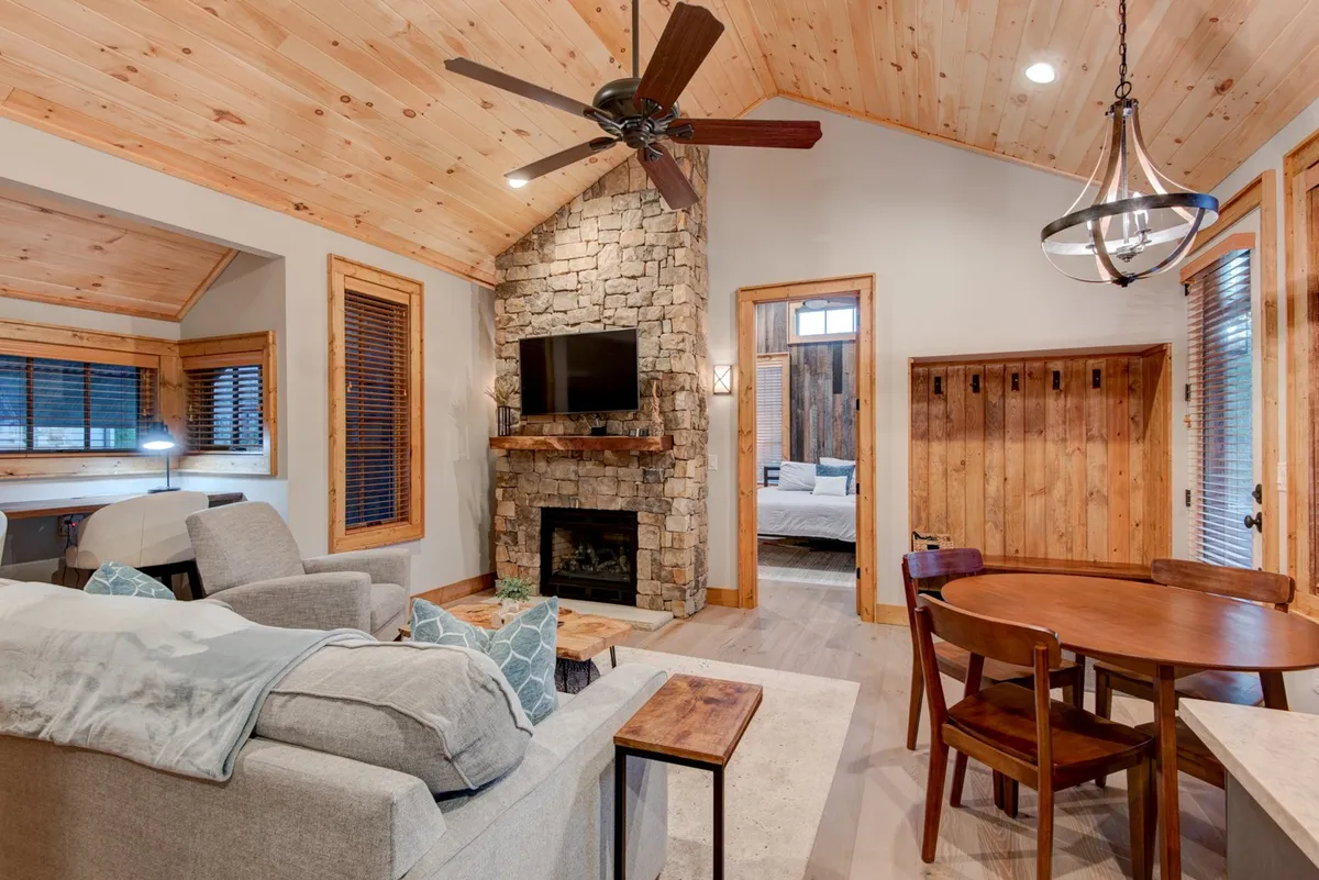 An inviting open-plan area where a plush sofa faces a large stone fireplace, adjacent to a wooden dining table. The seamless flow between the living and dining spaces encourages socializing, shared meals, and relaxing in comfort.