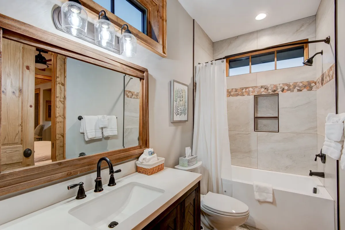 A serene bathroom scene with a modern vanity sink, a large framed mirror, a bathtub, and decorative tiles. The space feels open and step-free, ideal for guests with mobility needs.