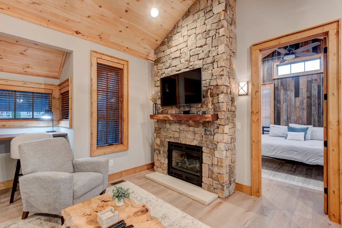 This interior image spotlights a warm stone fireplace with a comfortable armchair and natural wood accents. The TV mounted above the fireplace and soft lighting create a cozy retreat ideal for relaxing after outdoor adventures. The scene suggests a space where pets and owners can unwind together after a day of exploring.