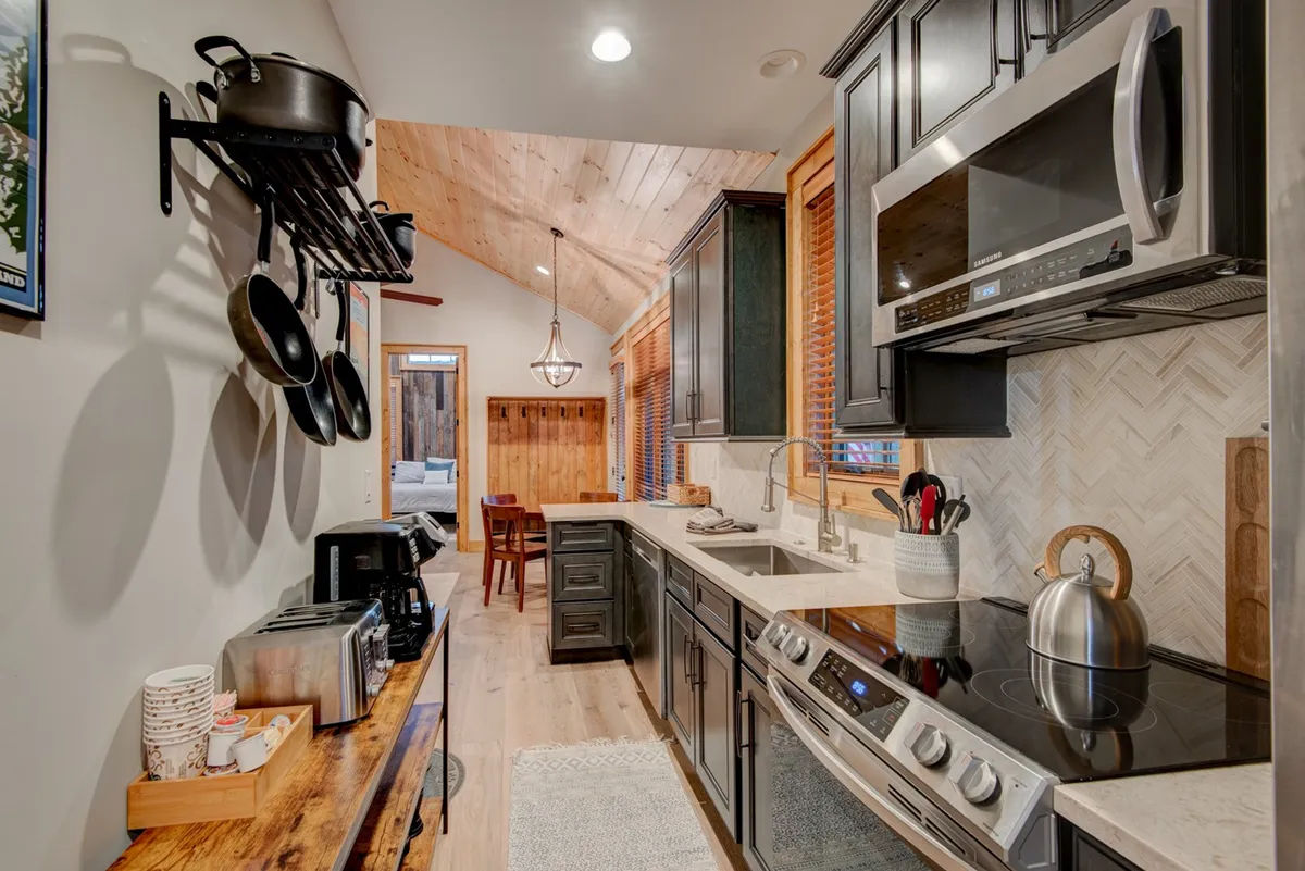 The kitchen is showcased with a central island, stainless steel appliances, wooden cabinetry, and hanging pots, all bathed in natural light from a large window. The arrangement suggests a practical, well-stocked space for meal prep and treat-making.