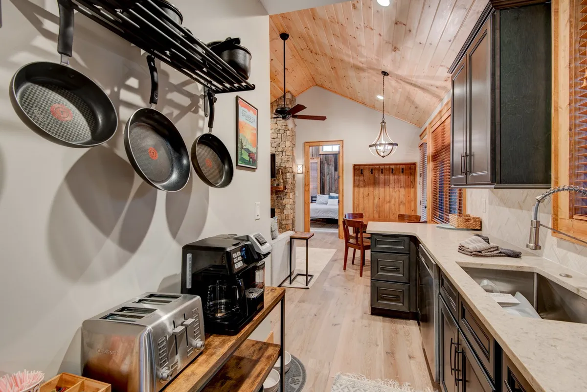 A view of a kitchen island with bar stools, hanging pots, and modern appliances, set against warm wooden cabinetry. The breakfast bar provides a casual spot for conversation, morning coffee, or informal dining, enhancing the sense of community.