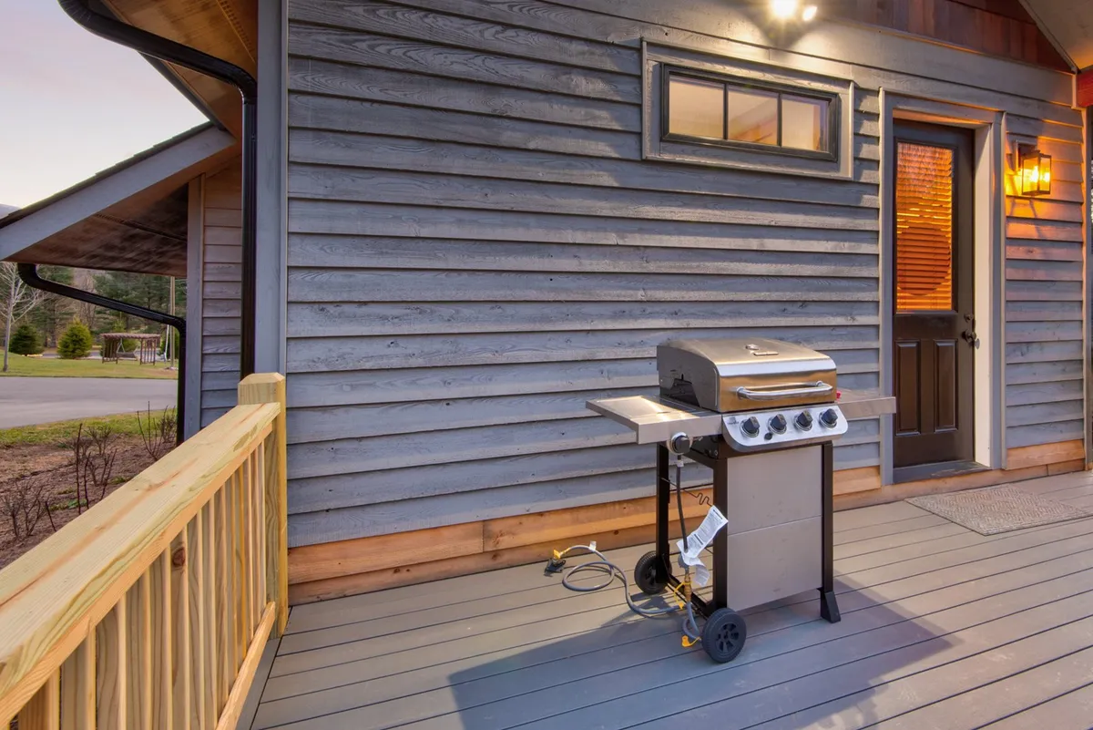 An inviting view of the outdoor deck area, emphasizing the grill, doorway, and wooden railing. The scene conveys a sense of relaxation and togetherness, with soft evening light suggesting the perfect place to recount the day's adventures.