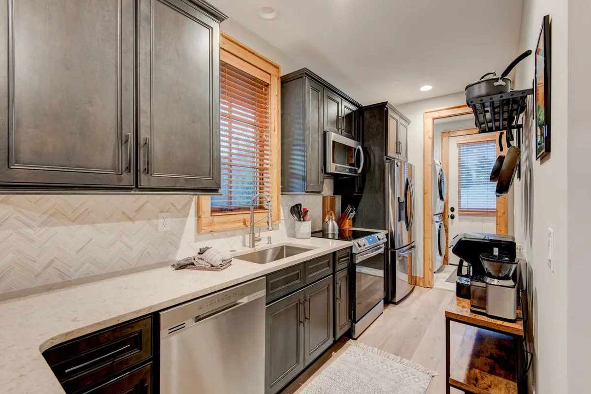 A modern kitchen with stainless steel appliances, a spacious island ideal for meal prep or casual chats, and warm wood accents that create a welcoming ambiance. The setup suggests ample room for multiple guests to interact, cook, or simply hang out.