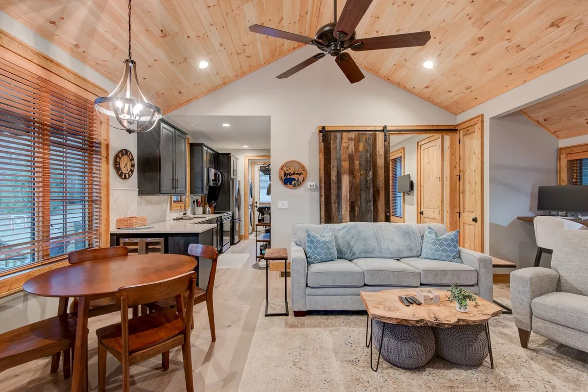 A cozy living and dining space featuring a plush sofa adorned with decorative cushions, a wooden dining table ready for group meals, and a stylish pendant light overhead. The open layout and inviting decor suggest a welcoming atmosphere for gatherings and shared moments.