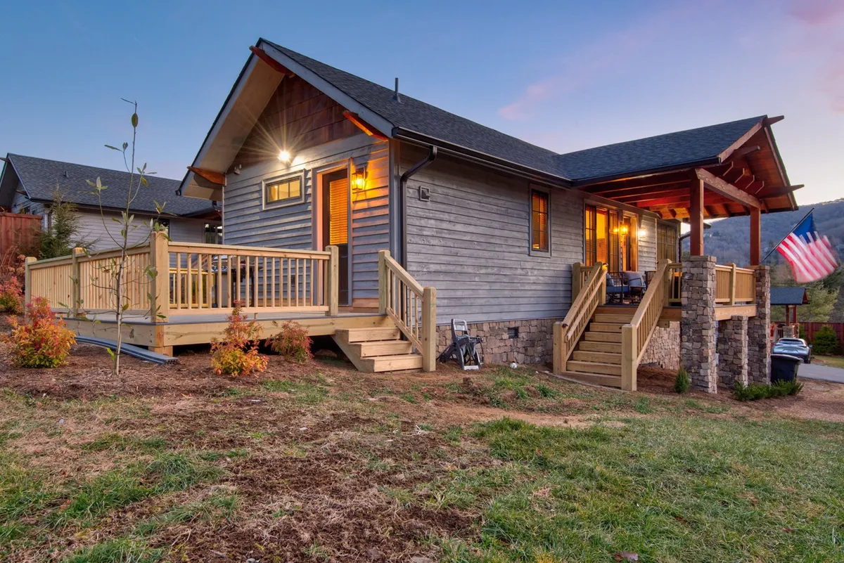 A broad view of the wooden deck accented with stone and decorative lighting, plus an American flag for a touch of personality. The spacious porch invites gatherings, relaxation, and offers a vista of the surrounding area.