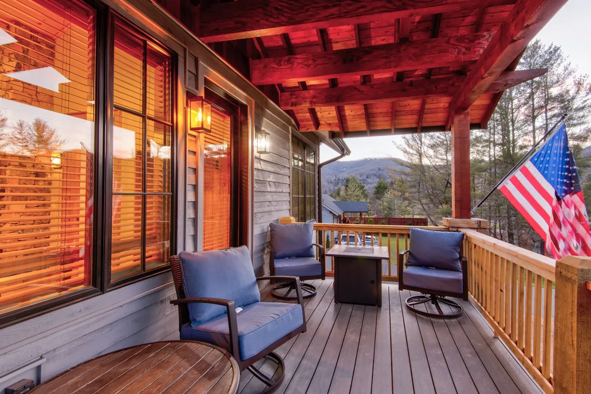 A cozy outdoor seating area is arranged around an outdoor table on the porch, flanked by the American flag. The scene is set for relaxing conversations, watching sunsets over the mountains, or planning the next day's adventures.