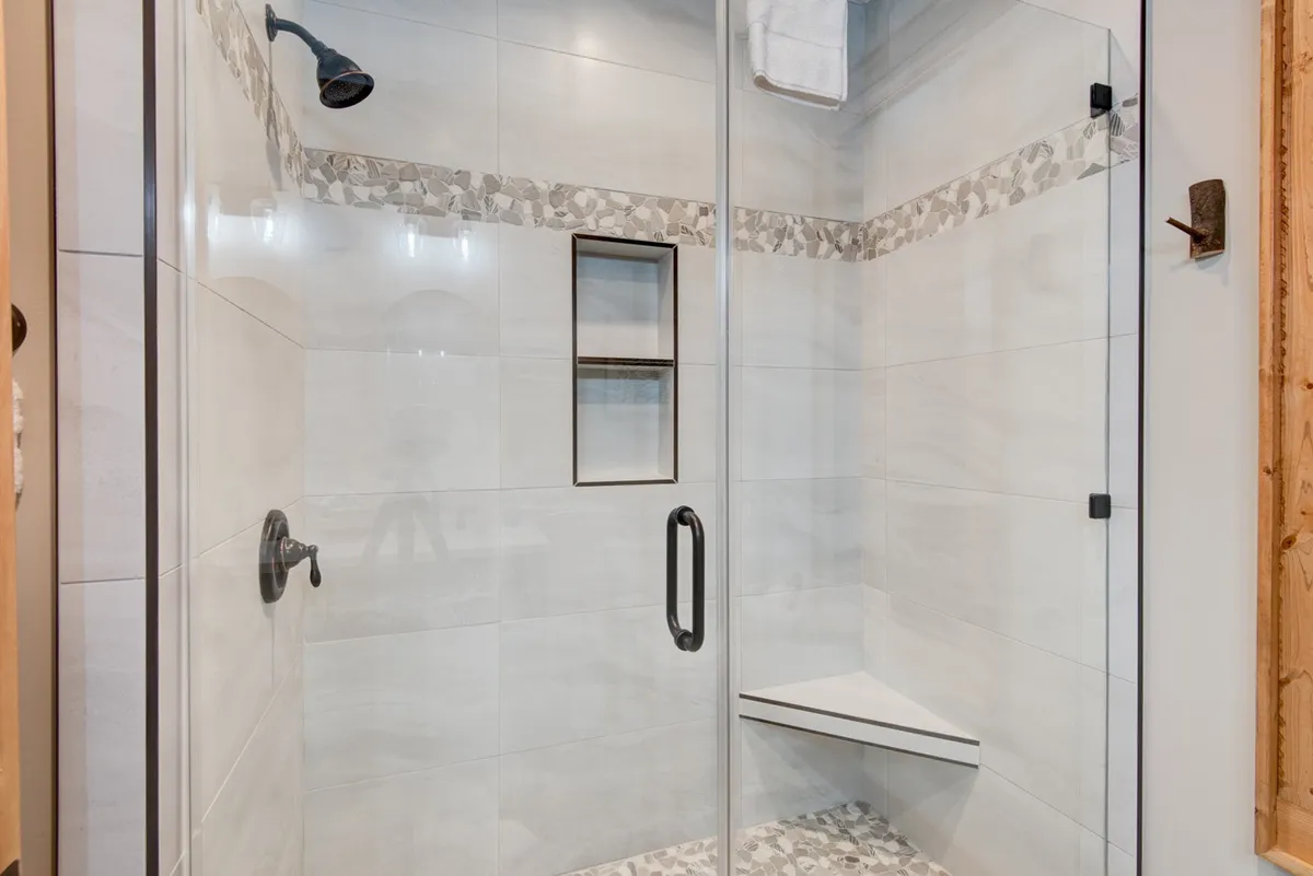 A modern bathroom featuring a glass-walled shower enclosure, decorative tile trim, and a sleek shower head. The space is bright and clean, designed for personal wellness and rejuvenation.