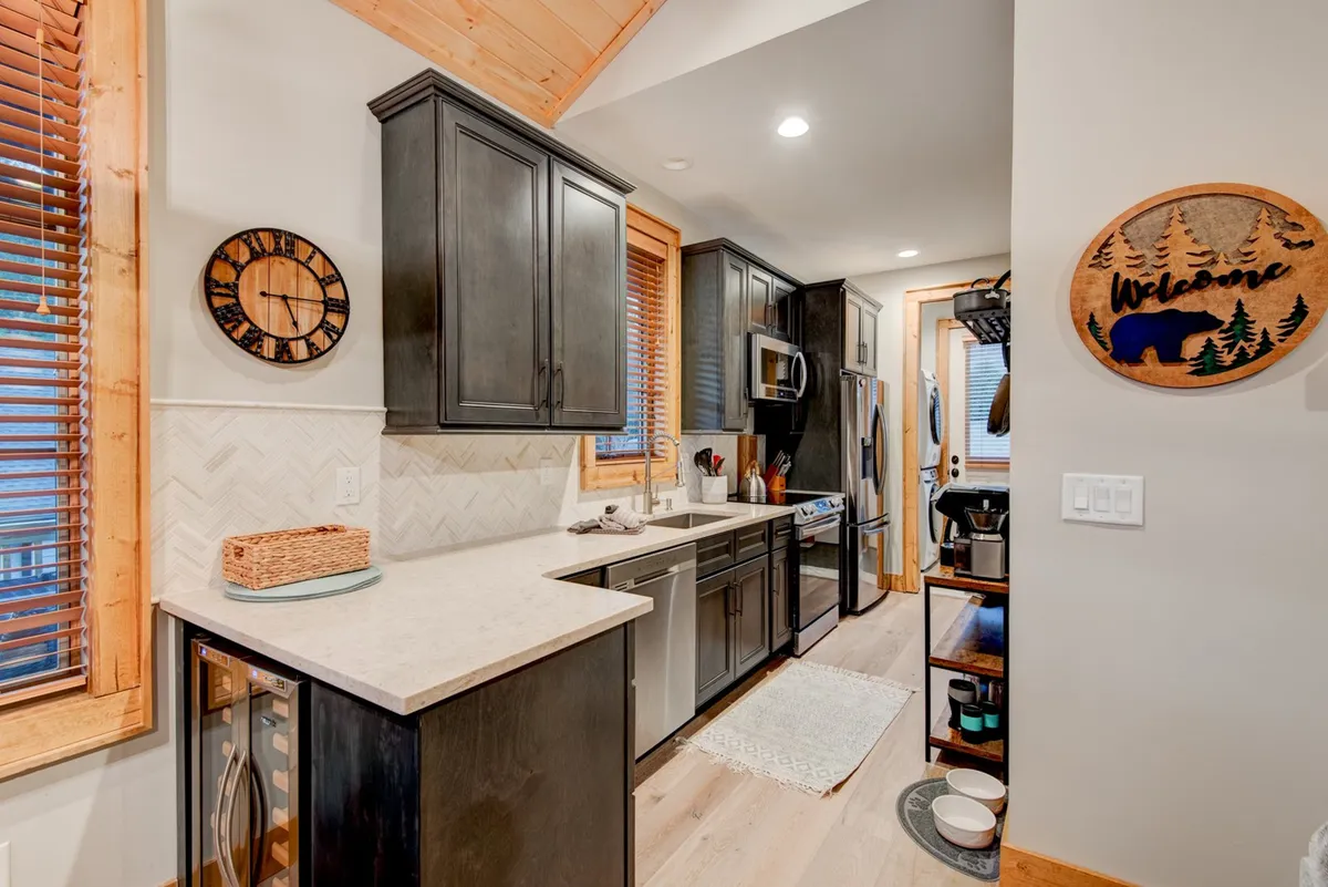 A cozy, welcoming kitchen nook with cabinetry, spacious countertops, a decorative clock, and a cheerful welcome sign. The space feels intimate yet open, inviting guests to connect over shared meals or casual conversation.